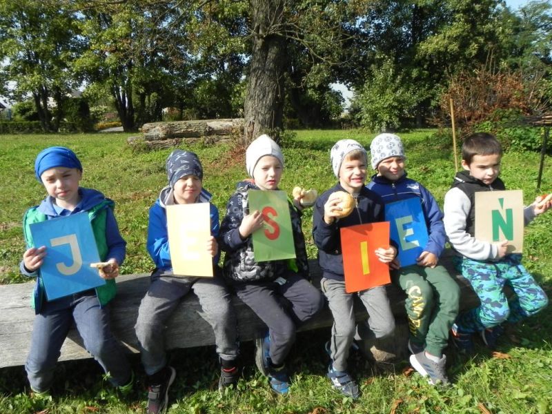 chłopcy siedzą i trzymają kartki z napisem jesień